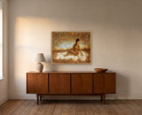 Transcendence by Frantisek Strouhal: seated woman in ochre haze above pale white mist, brown and blue sky, the 30 by 24 inch print in a pale oak floater frame, hanging above a walnut sideboard in a calm room, shown at its true size