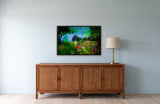Country Side by Frantisek Strouhal: two trees on a green hillside under a blue and green streaked sky, the 33 by 22 inch print in a black painted floater frame, hanging above a rattan and wood sideboard in a calm room, shown at its true size