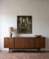 The Time Keeper by Frantisek Strouhal: a bearded man in a robe with arms outstretched and two faces behind him, the 24 by 30 inch print in a dark oak floater frame, hanging above a walnut sideboard in a calm room, shown at its true size