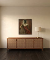 Graceful Pause by Frantisek Strouhal: a woman in a red satin dress seated, looking aside, warm brown ground, the 24 by 30 inch print in a dark oak floater frame, hanging above a rattan and wood sideboard in a calm room, shown at its true size