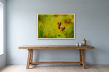 Pansies by Frantisek Strouhal: dark maroon blooms against blurred yellow and green foliage, the 33 by 22 inch print in a white painted floater frame, hanging above a elm console in a calm room, shown at its true size