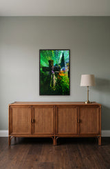 The Cross by Frantisek Strouhal: weathered stone cross with a church spire behind, green and blue washes, the 22 by 33 inch print in a black painted floater frame, hanging above a rattan and wood sideboard in a calm room, shown at its true size