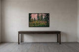 Idaho Peak by Frantisek Strouhal: red and purple wildflowers in a meadow below dark conifers and a pink slope, the 33 by 22 inch print in a black painted floater frame, hanging above a dark oak console table in a calm room, shown at its true size
