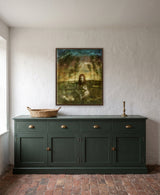 Rio by Frantisek Strouhal: a red-haired girl seated among thin trees under a teal and gold sky, the 24 by 30 inch print in a dark oak floater frame, hanging above a dark green sideboard in a calm room, shown at its true size
