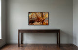 Autumn Leaves by Frantisek Strouhal: dried grasses and curled brown leaves against speckled blue and gold, the 33 by 22 inch print in a black painted floater frame, hanging above a dark oak console table in a calm room, shown at its true size