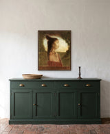 Being Mana by Frantisek Strouhal: young woman in profile with a shell earring and red wrap, green field behind, the 24 by 30 inch print in a dark oak floater frame, hanging above a dark green sideboard in a calm room, shown at its true size