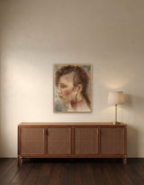The Golden Earring by Frantisek Strouhal: profile of a woman with a large gold hoop earring, soft browns and rose, the 24 by 30 inch print in a pale oak floater frame, hanging above a rattan and wood sideboard in a calm room, shown at its true size