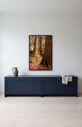 Cedar Grove by Frantisek Strouhal: pale tree trunks over speckled pink and black stone, rust and ochre tones, the 22 by 33 inch print in a black painted floater frame, hanging above a navy painted cupboard in a calm room, shown at its true size