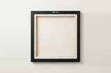 The back of the framed canvas: the canvas stretched over light wooden bars and stapled around the inner edge, one sawtooth hanger fitted to the top bar, and no bracing across the middle. The frame edge is black painted.