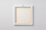 The back of the framed canvas: the canvas stretched over light wooden bars and stapled around the inner edge, one sawtooth hanger fitted to the top bar, and no bracing across the middle. The frame edge is white painted.
