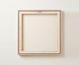 The back of the framed canvas: the canvas stretched over light wooden bars and stapled around the inner edge, one sawtooth hanger fitted to the top bar, and no bracing across the middle. The frame edge is pale oak.