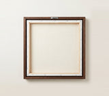 The back of the framed canvas: the canvas stretched over light wooden bars and stapled around the inner edge, one sawtooth hanger fitted to the top bar, and no bracing across the middle. The frame edge is dark oak.