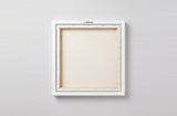 The back of the framed canvas: the canvas stretched over light wooden bars and stapled around the inner edge, one sawtooth hanger fitted to the top bar, and no bracing across the middle. The frame edge is white painted.