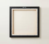 The back of the framed canvas: the canvas stretched over light wooden bars and stapled around the inner edge, one sawtooth hanger fitted to the top bar, and no bracing across the middle. The frame edge is black painted.