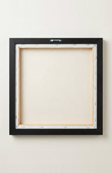 The back of the framed canvas: the canvas stretched over light wooden bars and stapled around the inner edge, one sawtooth hanger fitted to the top bar, and no bracing across the middle. The frame edge is black painted.