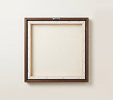The back of the framed canvas: the canvas stretched over light wooden bars and stapled around the inner edge, one sawtooth hanger fitted to the top bar, and no bracing across the middle. The frame edge is dark oak.