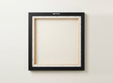 The back of the framed canvas: the canvas stretched over light wooden bars and stapled around the inner edge, one sawtooth hanger fitted to the top bar, and no bracing across the middle. The frame edge is black painted.