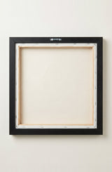 The back of the framed canvas: the canvas stretched over light wooden bars and stapled around the inner edge, one sawtooth hanger fitted to the top bar, and no bracing across the middle. The frame edge is black painted.