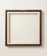 The back of the framed canvas: the canvas stretched over light wooden bars and stapled around the inner edge, one sawtooth hanger fitted to the top bar, and no bracing across the middle. The frame edge is dark oak.