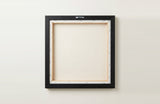 The back of the framed canvas: the canvas stretched over light wooden bars and stapled around the inner edge, one sawtooth hanger fitted to the top bar, and no bracing across the middle. The frame edge is black painted.