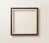 The back of the framed canvas: the canvas stretched over light wooden bars and stapled around the inner edge, one sawtooth hanger fitted to the top bar, and no bracing across the middle. The frame edge is dark oak.