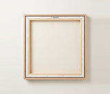 The back of the framed canvas: the canvas stretched over light wooden bars and stapled around the inner edge, one sawtooth hanger fitted to the top bar, and no bracing across the middle. The frame edge is pale oak.