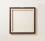 The back of the framed canvas: the canvas stretched over light wooden bars and stapled around the inner edge, one sawtooth hanger fitted to the top bar, and no bracing across the middle. The frame edge is dark oak.