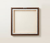 The back of the framed canvas: the canvas stretched over light wooden bars and stapled around the inner edge, one sawtooth hanger fitted to the top bar, and no bracing across the middle. The frame edge is dark oak.