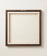 The back of the framed canvas: the canvas stretched over light wooden bars and stapled around the inner edge, one sawtooth hanger fitted to the top bar, and no bracing across the middle. The frame edge is dark oak.