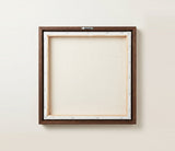 The back of the framed canvas: the canvas stretched over light wooden bars and stapled around the inner edge, one sawtooth hanger fitted to the top bar, and no bracing across the middle. The frame edge is dark oak.