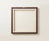 The back of the framed canvas: the canvas stretched over light wooden bars and stapled around the inner edge, one sawtooth hanger fitted to the top bar, and no bracing across the middle. The frame edge is dark oak.