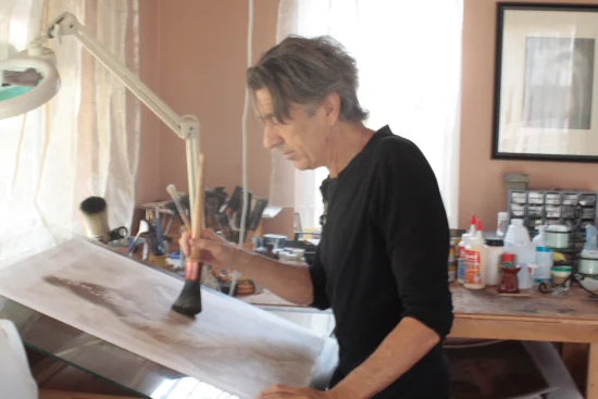 Frantisek at a lit drafting table, a stag-foot brush in his hand, working ink into a print